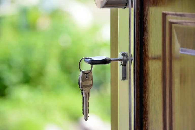 House keys inserted in a wooden door lock with a blurred garden background.