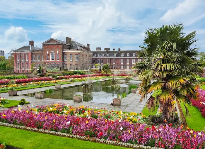 Kensington Palace sunken garden featuring colorful flower beds, a reflective pond, and palm trees.