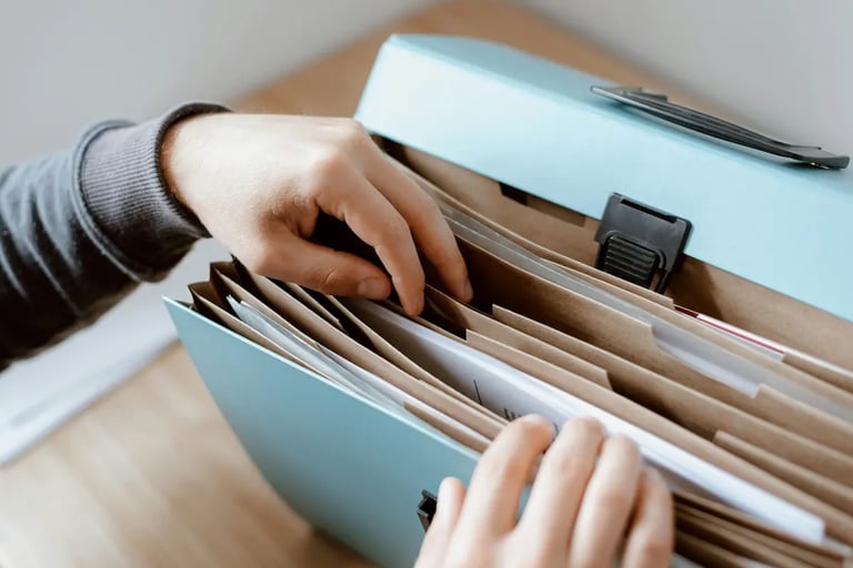 A person organizing business documents and paper files inside a light blue portable accordion folder.