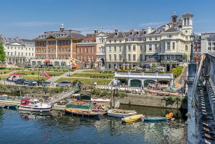Historic waterfront buildings and colorful boats docked along the River Thames in Richmond, London.