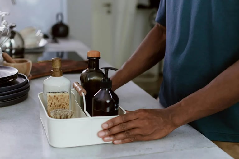 A person organizing reusable soap dispensers and cleaning tools in a white metal caddy.
