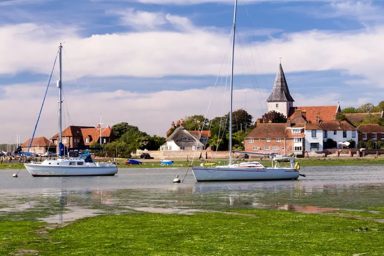 Sailboats moored in a coastal harbor near historic Rye village houses and a church.