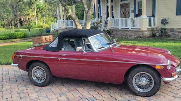 A sideview of a red MG MGB Roadster with black soft top.