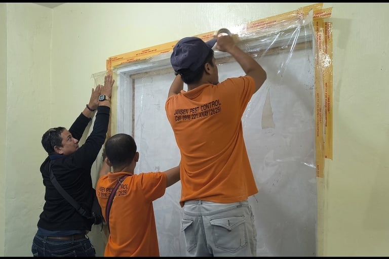Professional exterminators from Jansen Pest Control sealing a door with plastic for termite fumigation.