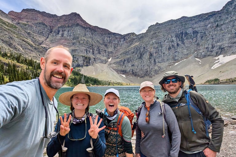 Hiking group smiling at Crypt Lake with mountain cliffs in Waterton Lakes National Park.