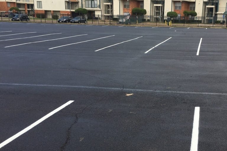 Freshly paved asphalt parking lot with white stripes in front of an apartment complex.