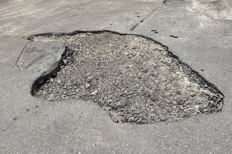 Large deep pothole in damaged asphalt road requiring professional pavement repair services.