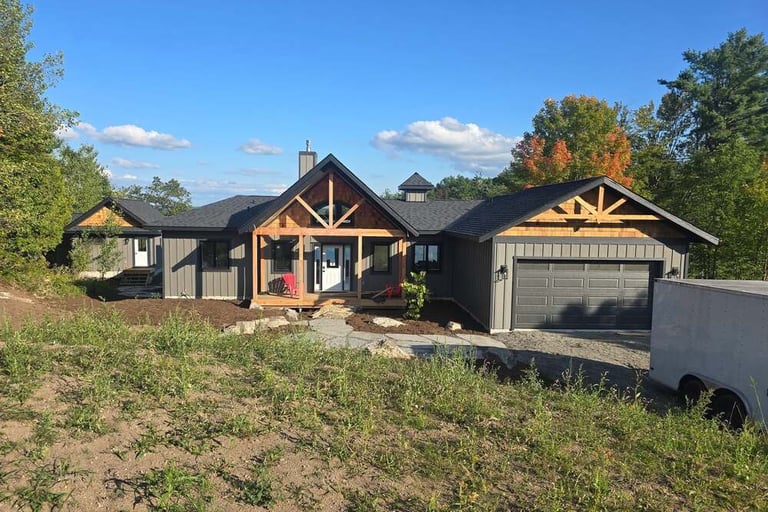 Modern rustic grey farmhouse with cedar wood accents, front porch, and garage under a blue sky.