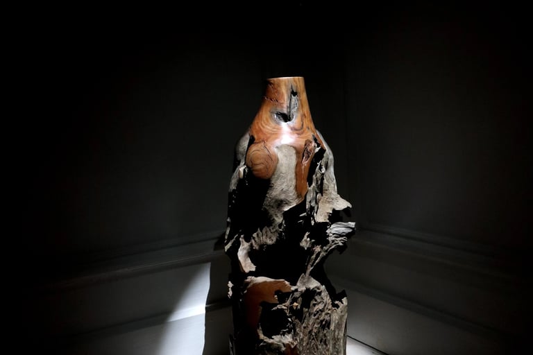 Rustic hand-carved natural wood sculpture spotlighted in a dark room as a piece of fine art decor.