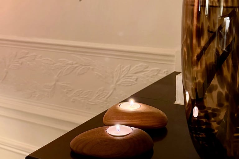 Two wooden pebble-shaped tea light candle holders on a dark table creating a cozy home atmosphere.