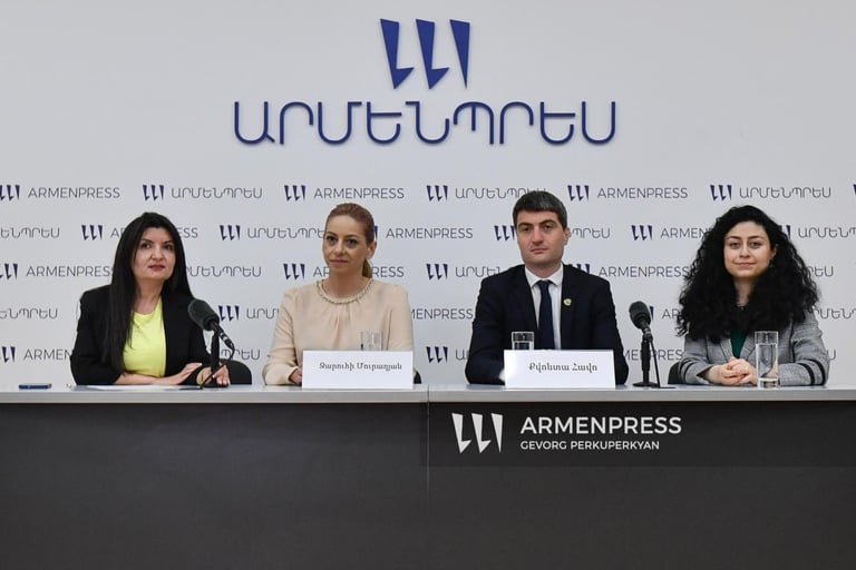 Four panelists seated at a table during an Armenpress news conference with microphones and nameplates.