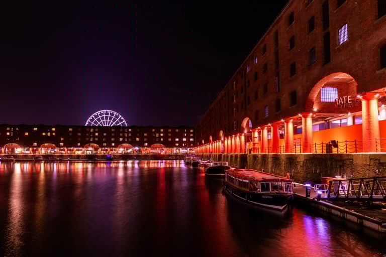 Night view of Liverpool Royal Albert Dock with red illuminated brick buildings and the illuminated Ferris wheel.