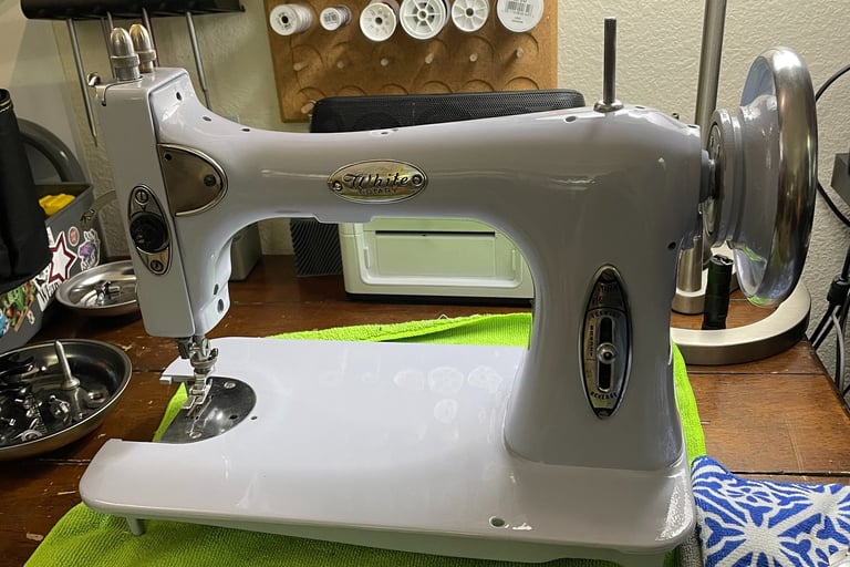 Vintage White sewing machine on a wooden workbench with thread spools and tools.