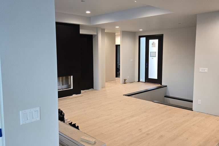Modern home interior renovation featuring light oak luxury vinyl plank flooring and black fireplace wall.