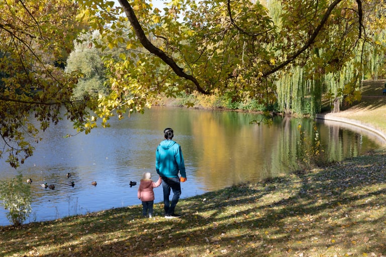 Bild von einer erwachsenen Person, die mit einem Kind an der Hand an einem See spazierengeht.