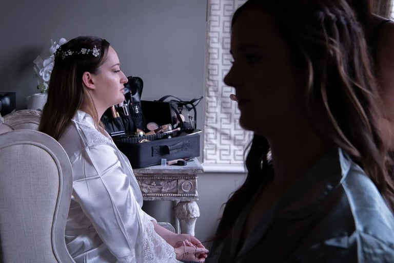 Bride in a white silk robe getting her wedding makeup done beside a professional cosmetic kit.