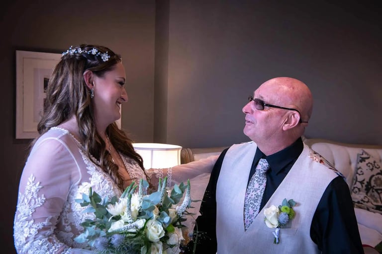Smiling bride in lace wedding dress holding a bouquet while looking at her father during a first look.