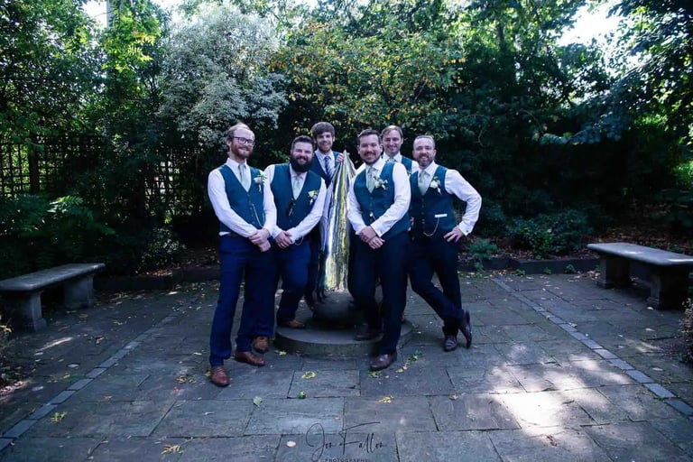 Groom and groomsmen in navy pants and teal vests posing in Abbey Gardens Bury St Edmunds.