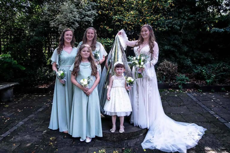 A bride in a white lace gown poses with bridesmaids in Abbey Gardens Bury St Edmunds.