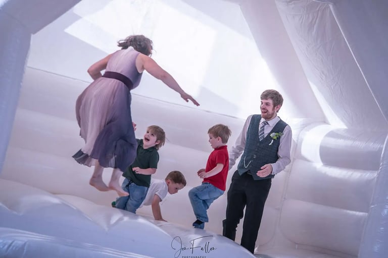 Wedding guests and children jumping inside a white inflatable bouncy castle at a wedding reception.
