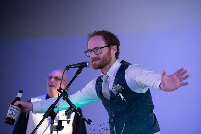 Groom in a green plaid waistcoat gives an energetic wedding speech holding a beer bottle at a microphone.