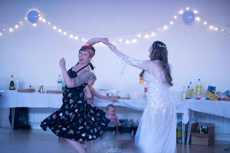 A bride and woman in a vintage dress dancing together at a wedding reception party.