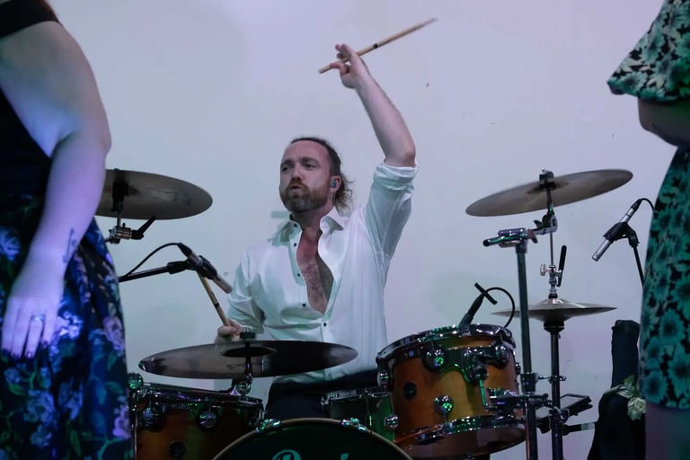 Professional male drummer playing an acoustic drum kit during a live musical performance.