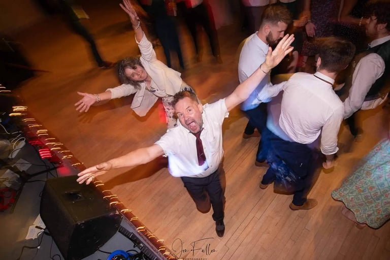 Wedding guests dancing and celebrating with arms raised on a crowded dance floor during a reception party.