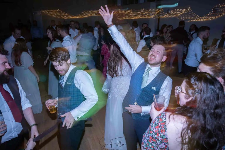 Wedding guests dancing and celebrating at a lively evening reception party.