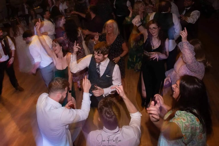 Wedding guests dancing and celebrating on a crowded dance floor during a lively reception party.