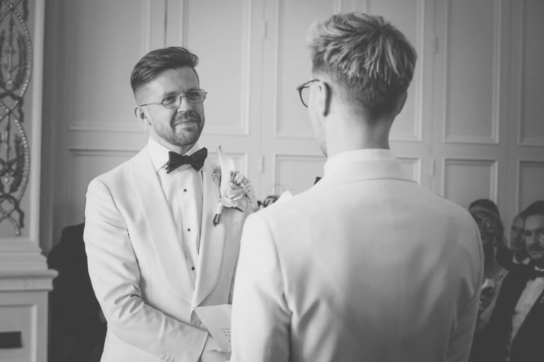 Groom in a white tuxedo exchanging vows at a black and white wedding ceremony.
