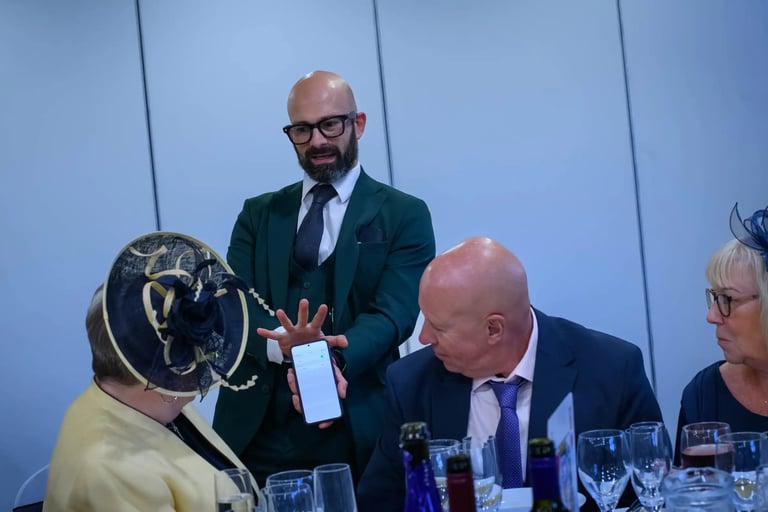 Professional magician in a green suit performing a digital phone trick for guests at a formal wedding reception.