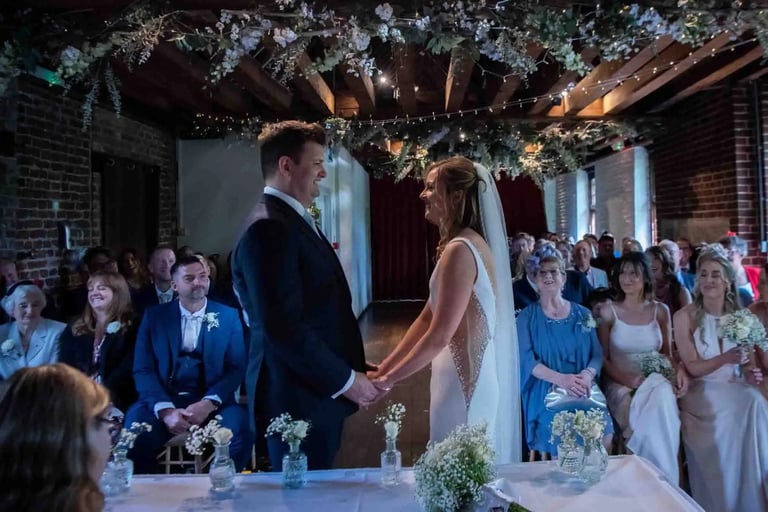 A bride and groom exchange vows in a rustic barn wedding ceremony venue with floral decor.
