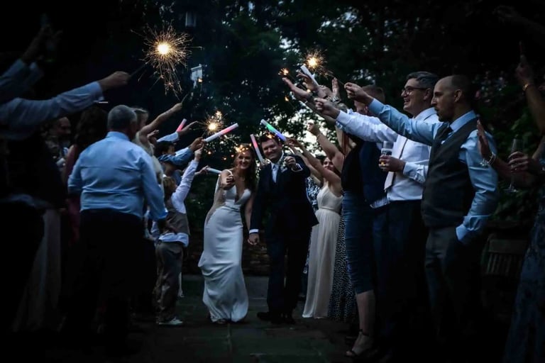 A bride and groom walk through a wedding sparkler send-off celebration at night.