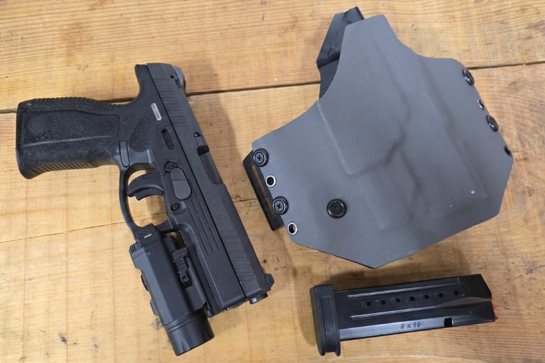Black Steyr L9-A2 MF handgun with mounted tactical light, gray Kydex holster, and 9mm magazine on a wood surface.