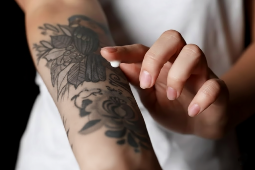 Aplicando crema hidratante de cuidado posterior para tatuajes sobre un nuevo tatuaje floral en negro