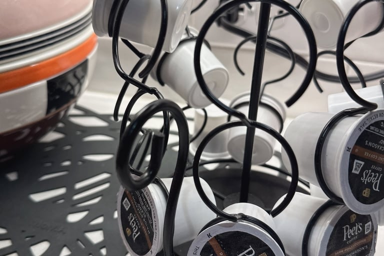 Black wire carousel organizer holding Peet's Coffee K-Cup pods on a white kitchen countertop.