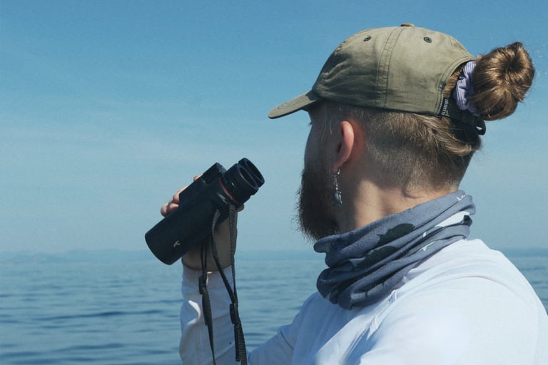 Scientist on a boat at sea using binoculars to spot cetaceans.