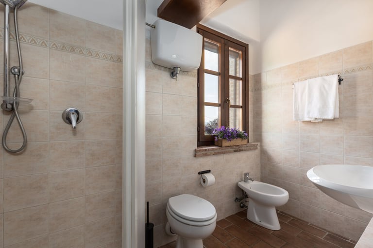 Modern rustic bathroom featuring beige tiles, walk-in shower, white bidet, and a wooden window.