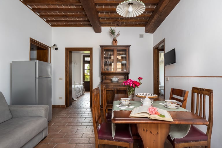 Rustic Italian kitchen and dining area featuring wooden ceiling beams, terracotta floors, and vintage furniture.
