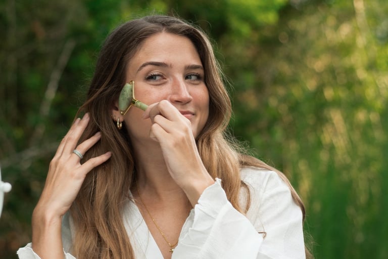 A woman using a green jade facial roller for her skincare routine at a vanity mirror outdoors.