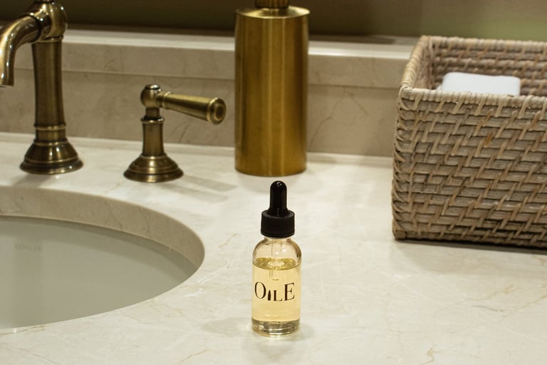 Glass bottle of luxury facial oil with dropper on a marble bathroom vanity next to gold fixtures.