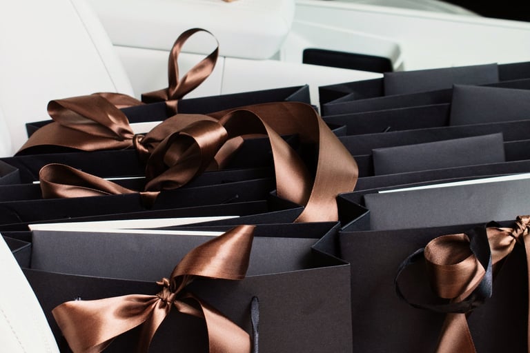 Luxury black shopping bags with satin brown ribbons on a white leather car seat.