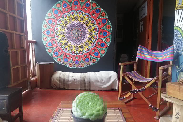 Sala con planta y mandala pintado en la pared, hay una silla mecedora y otros muebles rústicos con luz cálida