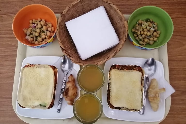Bandeja con almuerzo, lasaña con minicroisant, ensalada y limonada con cubiertos y servilletas
