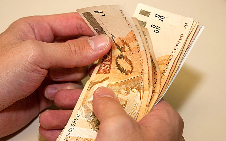 Pessoa contando notas de 50 rais