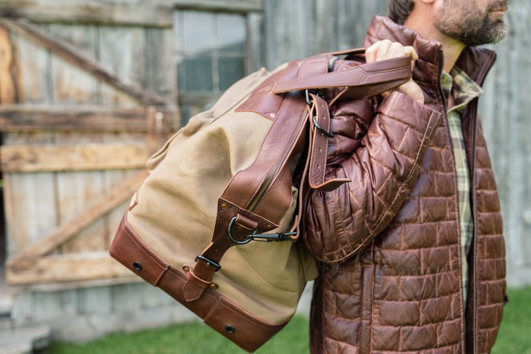 A man carrying a waxed canvas duffel bag over his shoulder while wearing a quilted brown jacket.
