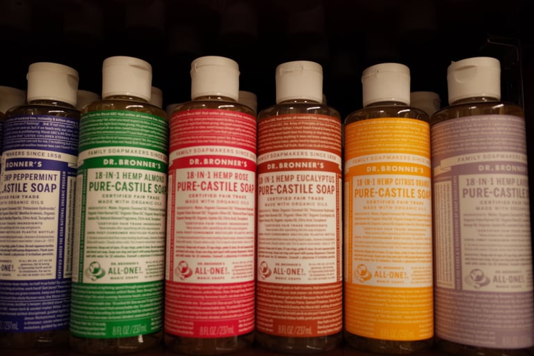 A row of various Dr. Bronner's Pure-Castile Soap bottles including Peppermint, Almond, Rose, and Citrus scents.