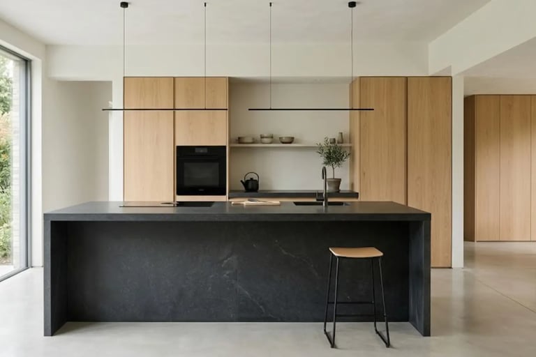 Cucina minimalista con isola in pietra scura, mobili in legno chiaro e linee essenziali