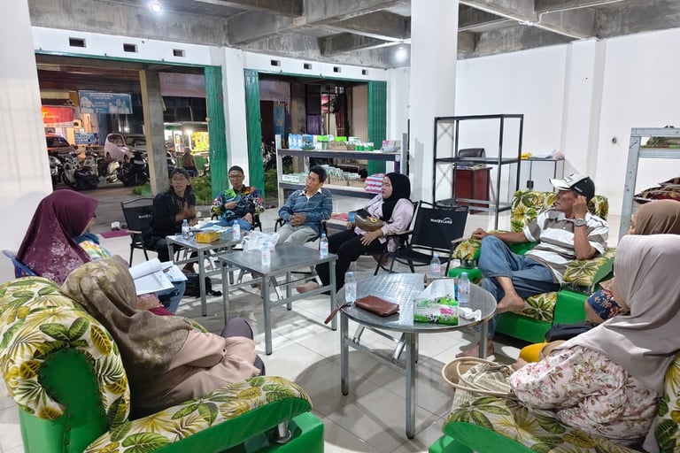 Community members gather for a formal meeting in a brightly lit room with green floral sofas.